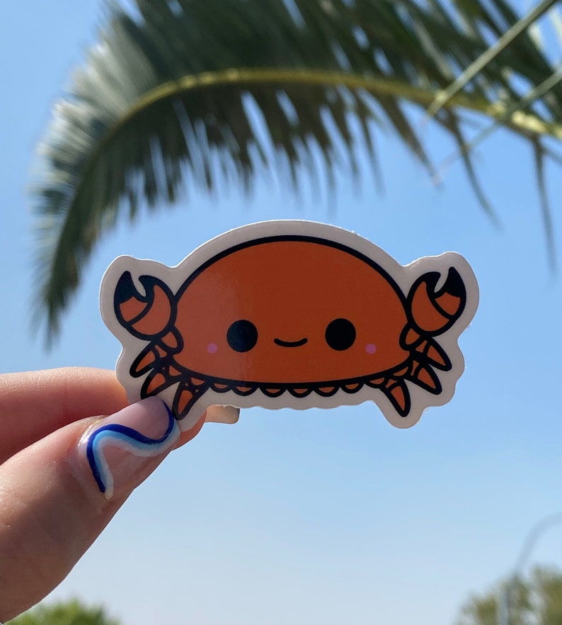 May include: A sticker of a cartoon crab with a smiling face. The crab is orange with black eyes and a black outline. The sticker is on a white background.