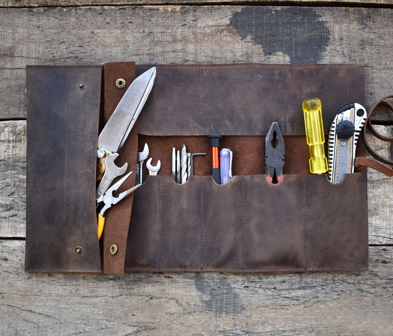 May include: A brown leather tool roll with multiple pockets and slots for holding tools. The roll is open and contains a variety of tools, including a knife, pliers, screwdrivers, and a utility knife.