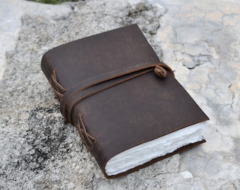 May include: A brown leather-bound journal with a white paper interior and a leather strap closure.