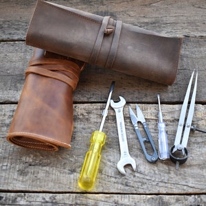 May include: A set of tools including a screwdriver, pliers, a compass, and a pair of scissors, all rolled up in a brown leather case.
