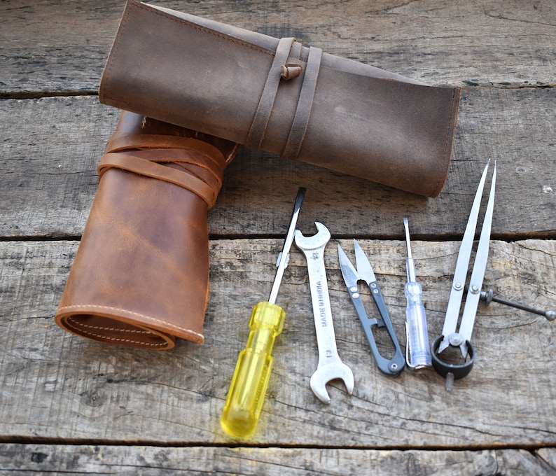 May include: A set of tools including a screwdriver, pliers, a compass, and a pair of scissors, all rolled up in a brown leather case.