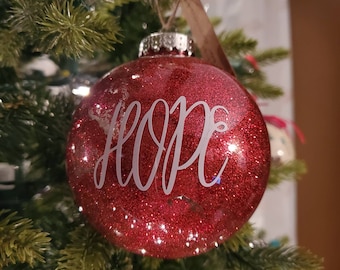 May include: Red glitter Christmas ornament with the word "HOPE" written in white lettering.