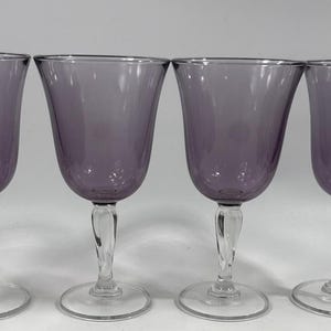 May include: Four purple wine glasses with clear, twisted stems and round bases. The glasses have a tulip-shaped bowl. The stems are clear and have a twisted design. The glasses are arranged in a row.