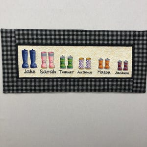 May include: A black and white checkered fabric with a row of colorful rain boots. The boots are labeled with the names Jake, Sarah, Tanner, Autumn, Mason, and Jackson.
