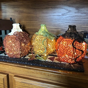 May include: Three crocheted pumpkin-shaped lamps with intricate designs and warm white lights. The pumpkins are in shades of orange, yellow, and green.