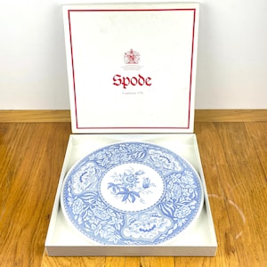 May include: A Spode plate with a blue floral design, presented in its original box. The plate has a central floral bouquet and detailed patterns. The box is white with red trim and the Spode logo.
