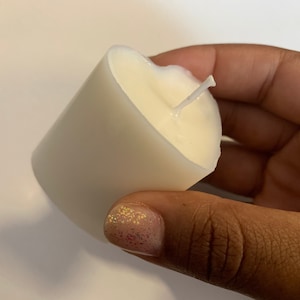May include: A white pillar candle with a single wick. The candle is in a person's hand.