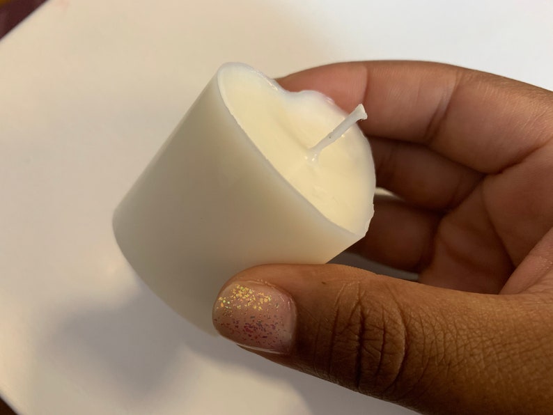 May include: A white pillar candle with a single wick. The candle is in a person's hand.