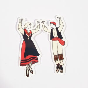 May include: A sticker featuring two figures in traditional Basque attire, a woman and a man, in a dancing pose. The woman wears a black and red dress, while the man is in white pants, a black vest, and a red sash. Both are outlined in black.