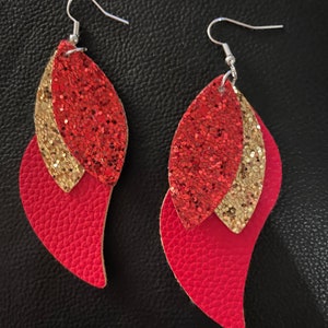 May include: A pair of dangle earrings with three layers of red and gold glitter leather. The top layer is gold glitter, the middle layer is red glitter, and the bottom layer is solid red leather.