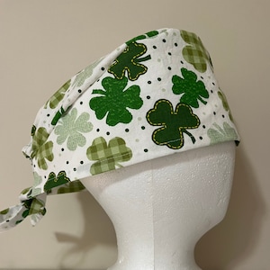 Peut inclure: Un bonnet de travail blanc avec un motif de trèfles verts. Le bonnet a une attache qui peut être nouée à l'arrière de la tête.