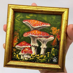 May include: A framed painting of red and white mushrooms in a forest setting. The painting is done in a realistic style with oil paints.