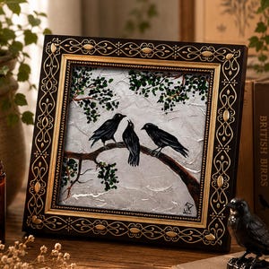 May include: A square painting in a dark ornate frame with gold accents, depicting three black crows perched on a brown tree branch against a textured white background with green leaves. The artist's initials JK are visible in the bottom right corner.