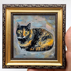 Könnte beinhalten: Gerahmtes Ölgemälde einer Schildpattkatze. Die Katze ist in Schwarz-, Orange- und Gelbtönen dargestellt, mit detailliertem Fellmuster. Der Rahmen ist verziert, mit einem goldenen Innenrand und einem dunkelbraunen Außenrand.