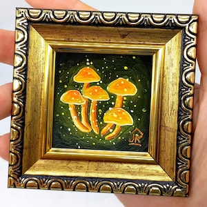 May include: A small framed painting of orange mushrooms on a green background with white speckles. The frame is gold with a black and gold ornate design.