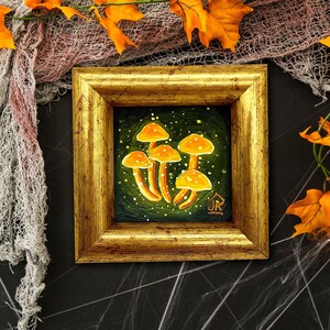 May include: A framed painting of orange mushrooms on a green background with white speckles. The frame is gold with a raised edge.