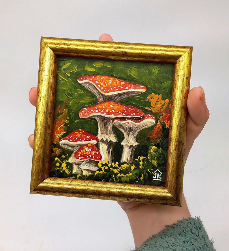 May include: A framed painting of red and white mushrooms in a forest setting. The painting is done in a realistic style with oil paints.