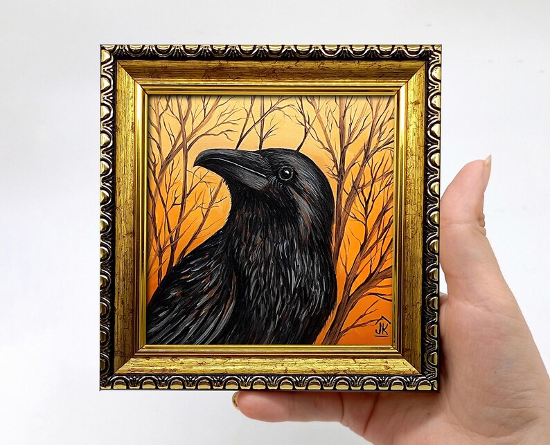Pode incluir: Pintura emoldurada de um corvo preto com penas detalhadas, contra um fundo de &aacute;rvores nuas e c&eacute;u laranja. A obra de arte est&aacute; fechada em uma moldura dourada ornamentada, criando uma est&eacute;tica vintage.
