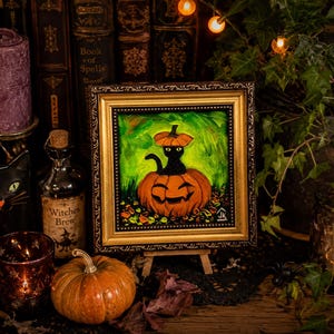 Op de afbeelding: Een ingelijst olieverfschilderij met een zwarte kat die in een uitgesneden oranje pompoen zit en een kleine pompoen als hoed draagt. Het kunstwerk is geplaatst tegen een levendige groene achtergrond met herfstbladeren aan de basis.