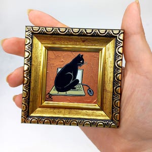 May include: A black cat sits on a laptop computer with a mouse on a brown background. The painting is framed in a gold frame.