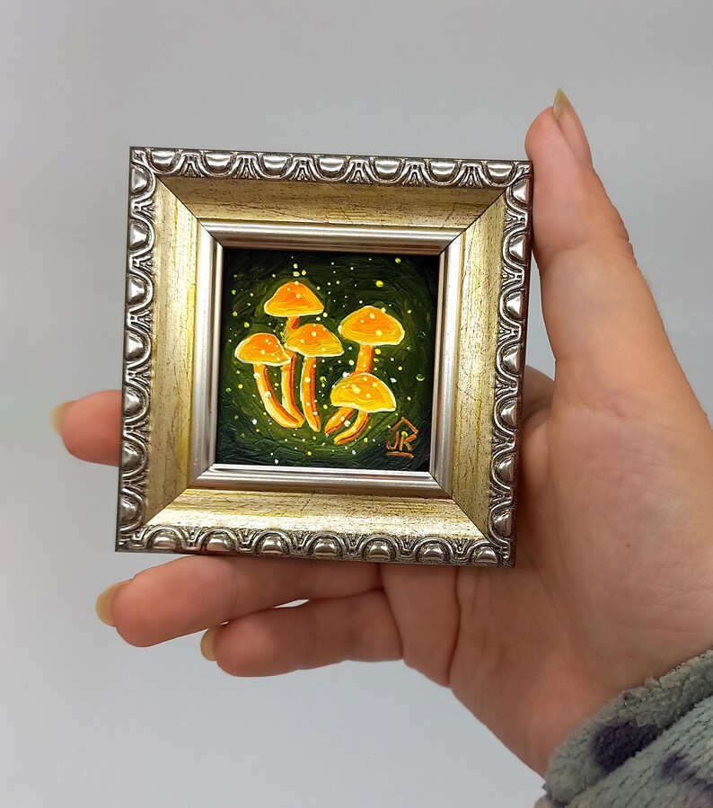 May include: A framed miniature painting of a cluster of glowing yellow mushrooms on a dark green background with white speckles. The painting is signed "JR" in the bottom right corner.