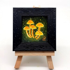 May include: A small framed painting of a cluster of yellow mushrooms on a green background with white speckles. The painting is on a small wooden easel.