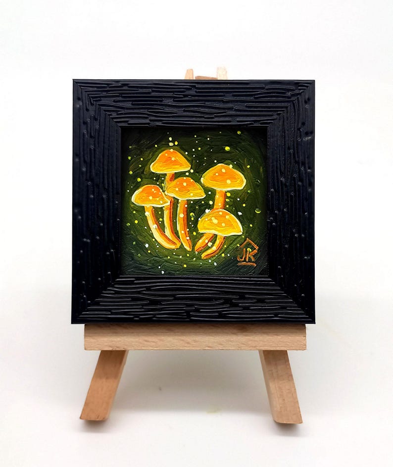 May include: A small framed painting of a cluster of yellow mushrooms on a green background with white speckles. The painting is on a small wooden easel.