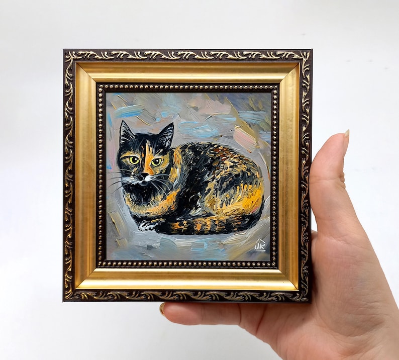 Pode incluir: Uma pintura a &oacute;leo de um gato tartaruga com pelagem preta e laranja, representado em posi&ccedil;&atilde;o sentada. A obra est&aacute; emoldurada numa moldura decorativa dourada e castanho-escura com detalhes em relevo nas bordas e uma borda interna de contas.