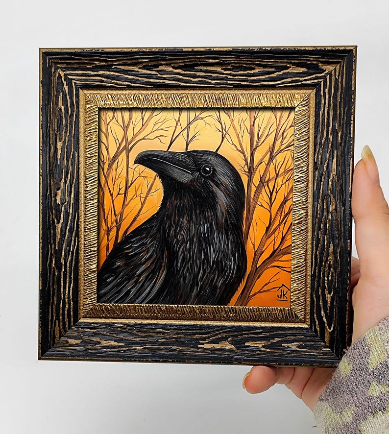 Pode incluir: Pintura emoldurada de um corvo preto com detalhes de penas, em um fundo laranja e marrom de &aacute;rvores nuas. A moldura &eacute; preta com detalhes dourados.