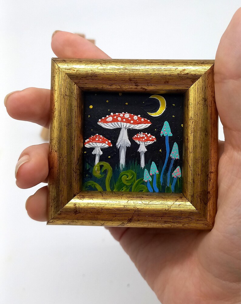 May include: A framed painting depicting a whimsical forest scene with red and white mushrooms, blue mushrooms, and a crescent moon in a starry night sky.