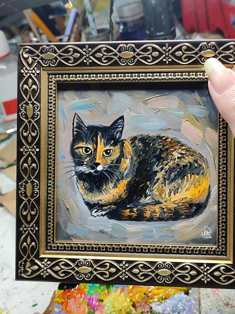 Pode incluir: Uma pintura a &oacute;leo de um gato tartaruga com pelagem preta e laranja e olhos amarelos, sobre um fundo cinza texturizado. A obra de arte est&aacute; emoldurada em uma moldura ornamentada marrom escura e dourada com padr&otilde;es de filigrana complexos.