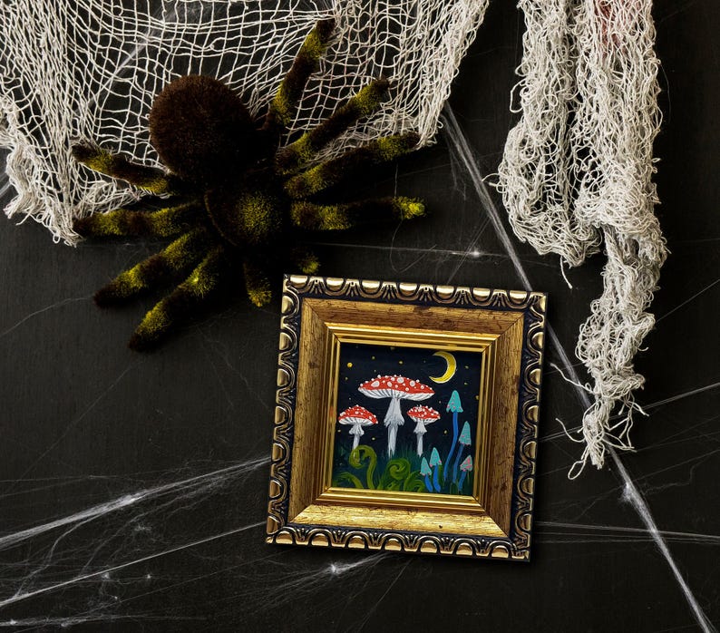May include: A framed painting depicting a whimsical forest scene with mushrooms, a crescent moon, and stars. The mushrooms are red and white with white spots, and the background is a dark blue.