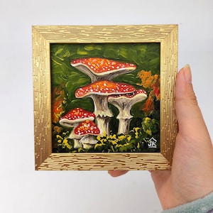 May include: A framed painting of red and white mushrooms with green foliage in the background. The painting is signed "JK" in the bottom right corner.
