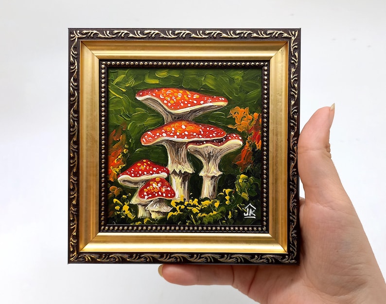 May include: A framed painting of red and white mushrooms in a forest setting. The mushrooms are painted in a realistic style with a textured brushstroke. The painting is framed in a gold and brown frame.