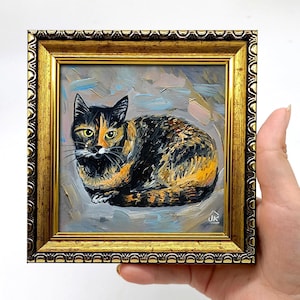 Pode incluir: Uma pintura a &oacute;leo de um gato tartaruga com pelagem preta, laranja e branca, retratado em posi&ccedil;&atilde;o sentada. A obra est&aacute; emoldurada numa moldura dourada ornamentada com uma borda texturizada. As iniciais do artista JK s&atilde;o vis&iacute;veis em branco.