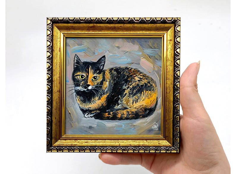 Pode incluir: Uma pintura a &oacute;leo de um gato tartaruga com pelagem preta, laranja e branca, retratado em posi&ccedil;&atilde;o sentada. A obra est&aacute; emoldurada numa moldura dourada ornamentada com uma borda texturizada. As iniciais do artista JK s&atilde;o vis&iacute;veis em branco.
