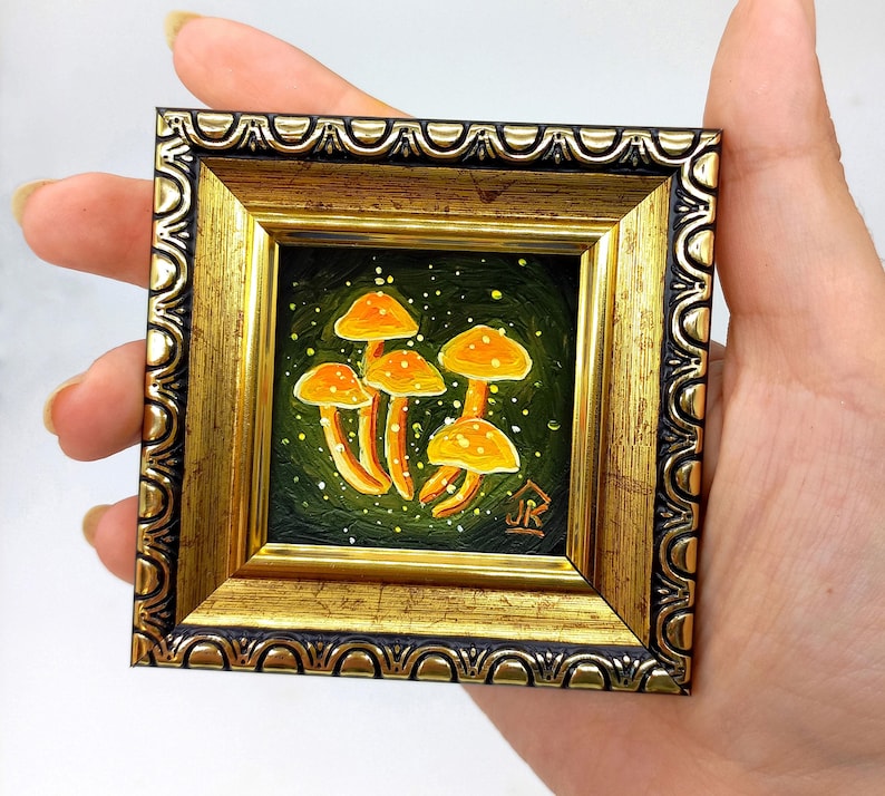May include: A small framed painting of orange mushrooms on a green background with white speckles. The frame is gold with a black and gold ornate design.
