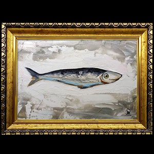Puede incluir: Una pintura enmarcada de un pez plateado con una franja azul sobre un fondo blanco con pinceladas grises y marrones. La pintura est&aacute; en un marco dorado con un borde decorativo.