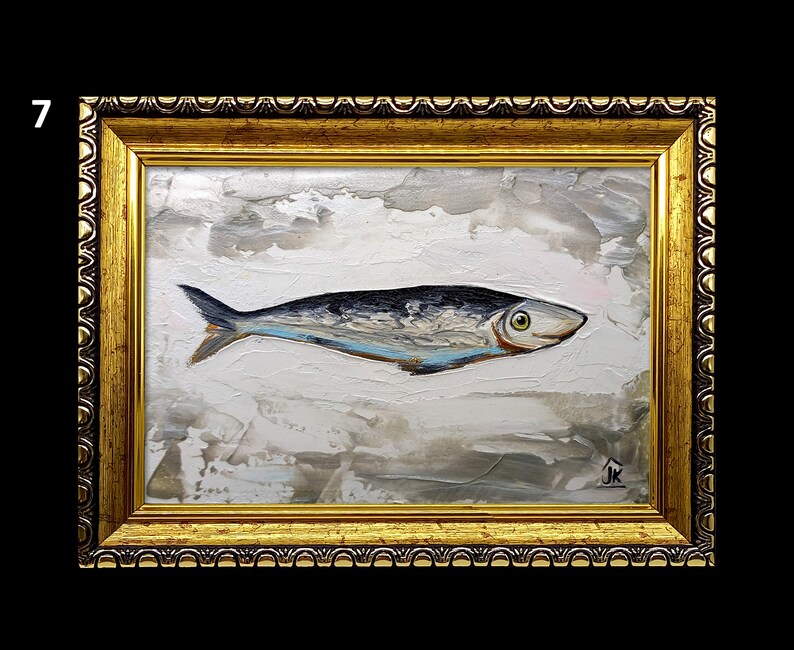 Puede incluir: Una pintura enmarcada de un pez plateado con una franja azul sobre un fondo blanco con pinceladas grises y marrones. La pintura est&aacute; en un marco dorado con un borde decorativo.