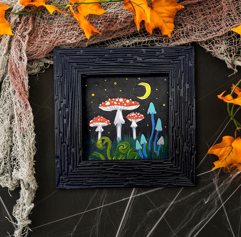 May include: A framed painting depicting a whimsical forest scene with red and white mushrooms, blue and green plants, and a crescent moon in the night sky.