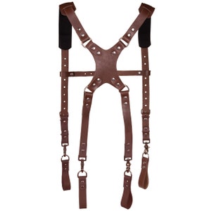 May include: Brown leather camera strap with adjustable straps and metal rings. The strap has a padded shoulder section and is designed for carrying a camera.