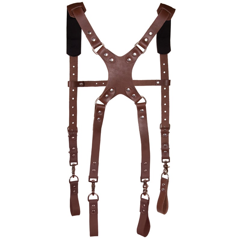 May include: Brown leather camera strap with adjustable straps and metal rings. The strap has a padded shoulder section and is designed for carrying a camera.