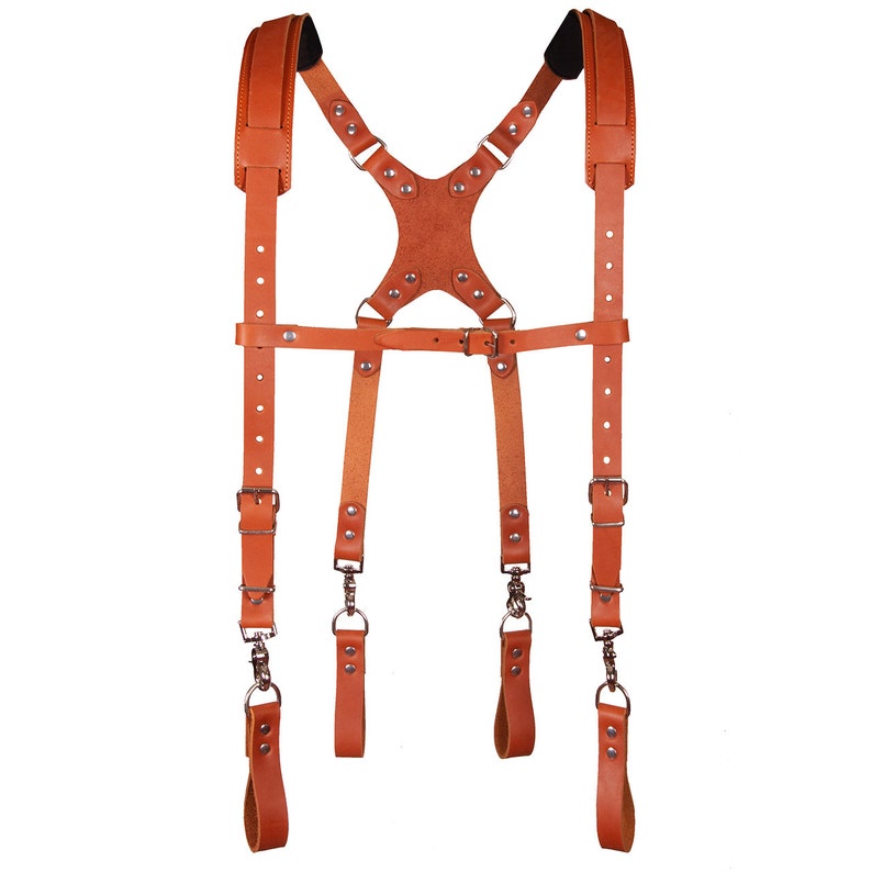 May include: A brown leather camera strap with adjustable straps and metal buckles. The strap is designed to be worn over the shoulders and has a chest strap for added support.