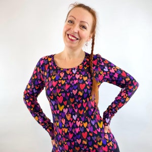 Könnte beinhalten: Ein langärmliges Shirt mit schwarzem Hintergrund und einem bunten Muster aus Herzen. Die Herzen sind in verschiedenen Schattierungen von Rosa, Lila, Rot, Orange und Gelb.