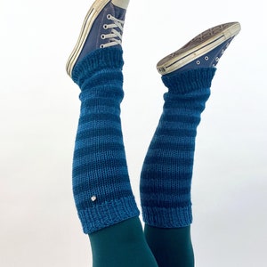 Puede incluir: Un par de polainas a rayas azules y verde azulado con un peque&ntilde;o bot&oacute;n plateado en la polainas izquierda. Las polainas se llevan sobre unos leggings de color verde azulado y unas zapatillas Converse azules.