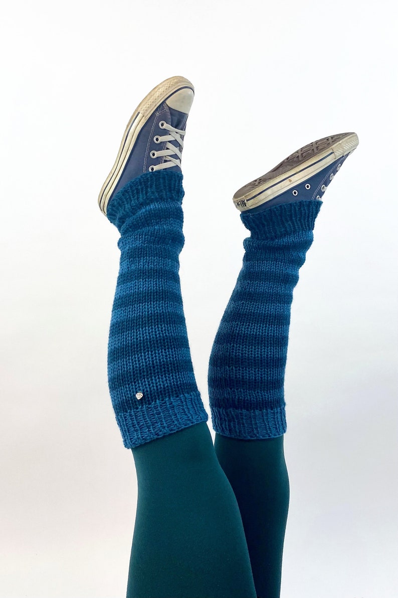 Puede incluir: Un par de polainas a rayas azules y verde azulado con un peque&ntilde;o bot&oacute;n plateado en la polainas izquierda. Las polainas se llevan sobre unos leggings de color verde azulado y unas zapatillas Converse azules.