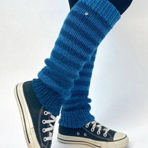 Puede incluir: Calentadores de piernas azules a rayas hechos de tejido de punto. Los calentadores de piernas se llevan sobre leggings negros y zapatillas negras.