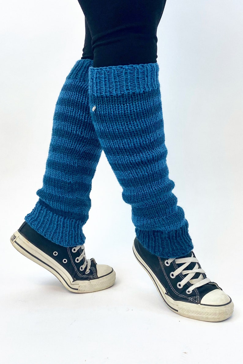 Puede incluir: Un par de polainas de punto azul con un patr&oacute;n de rayas. Las polainas se llevan sobre unos leggings negros y unas zapatillas negras.