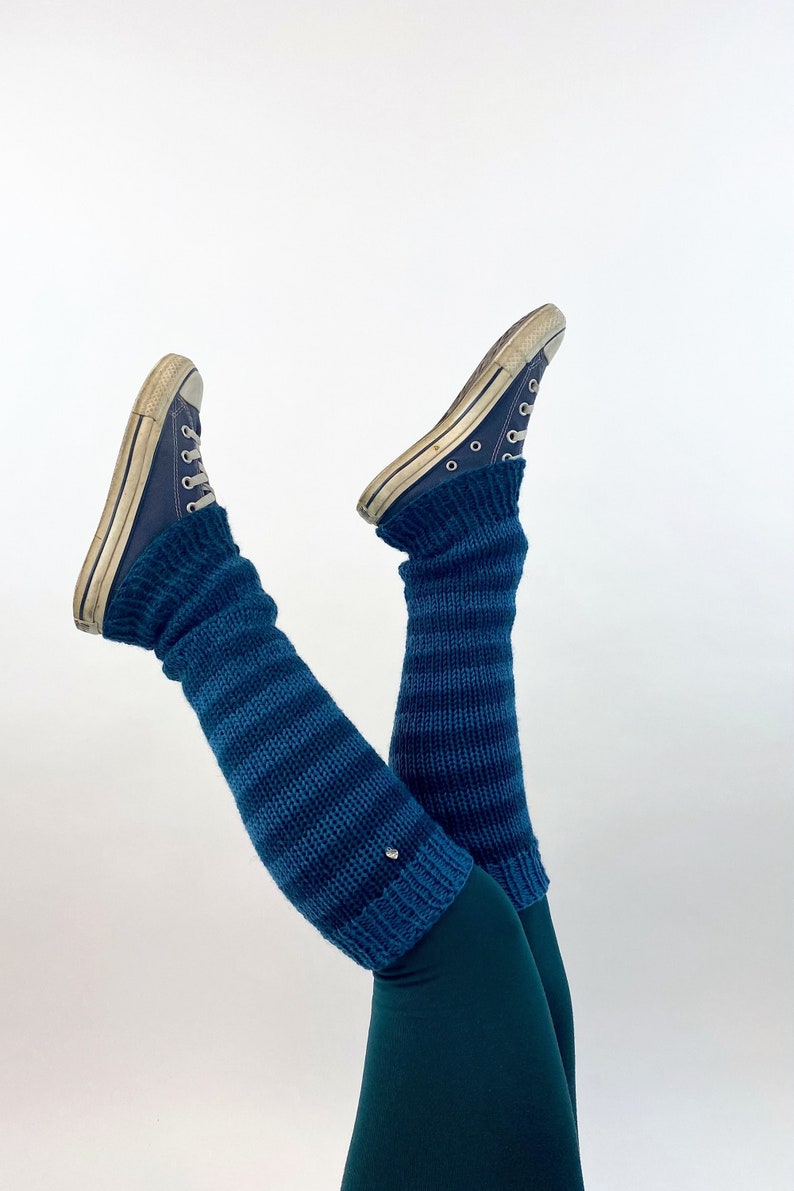 Puede incluir: Un par de polainas rayadas azules con un par de zapatillas Converse azules. Las polainas se llevan sobre unos leggings verde oscuro.
