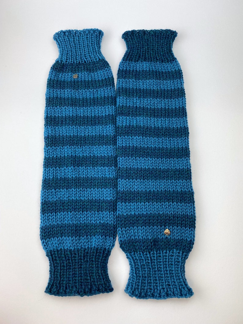 Puede incluir: Un par de polainas de punto a rayas azules y verde azulado con un peque&ntilde;o bot&oacute;n dorado en cada una.